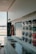 A modern interior with a sleek, glossy cabinet and a display of colorful samples on the wall. The setting is well-lit with natural light coming through a large window, and the decor is minimalistic and polished.