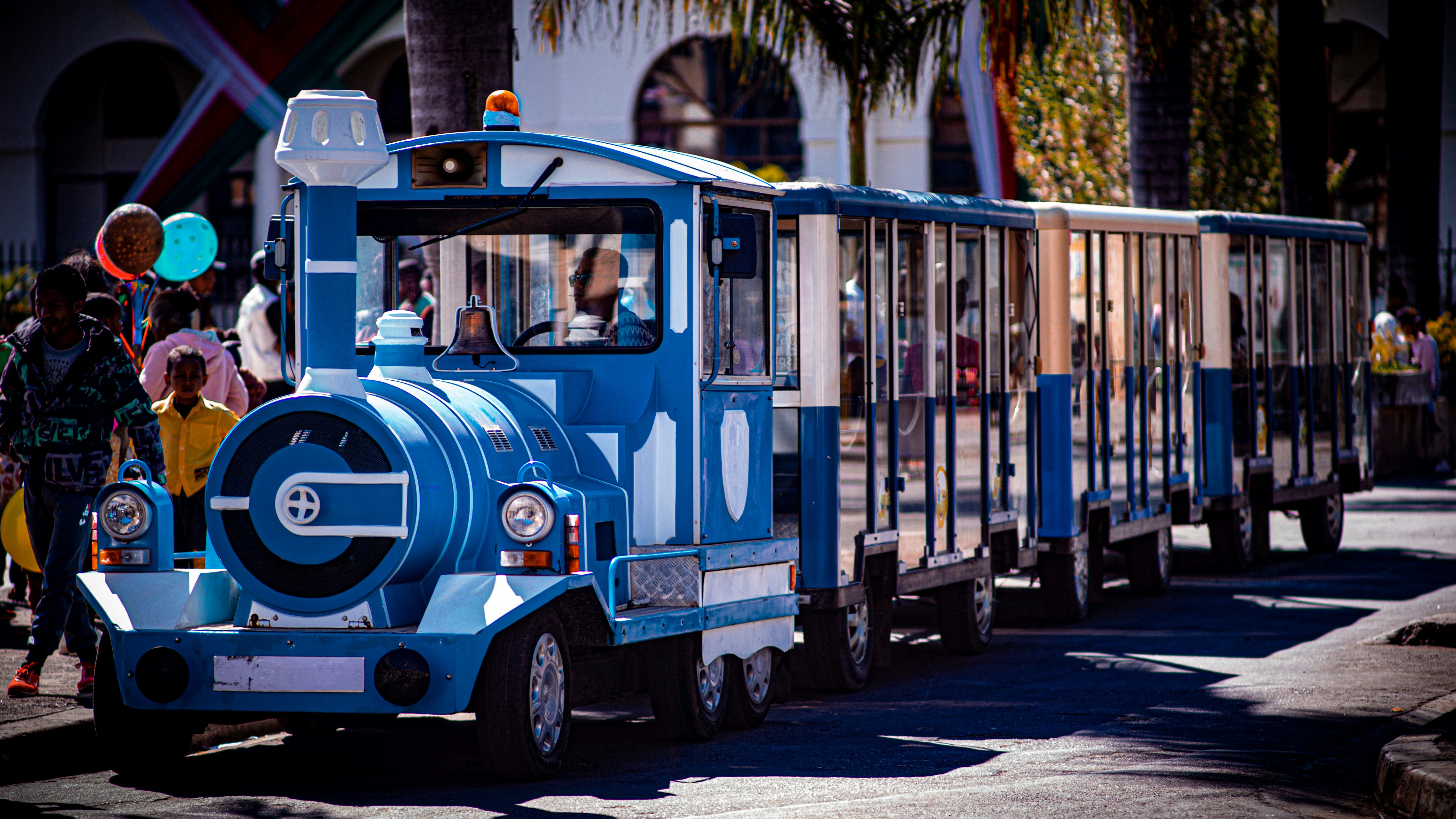 a small blue train is traveling down the street