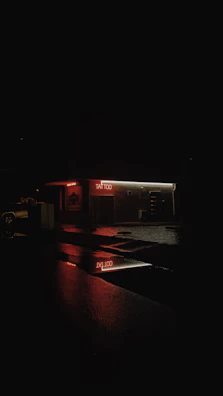 Neon-lit tattoo studio corner with bold black walls and a glowing red sign reflecting on polished surfaces.