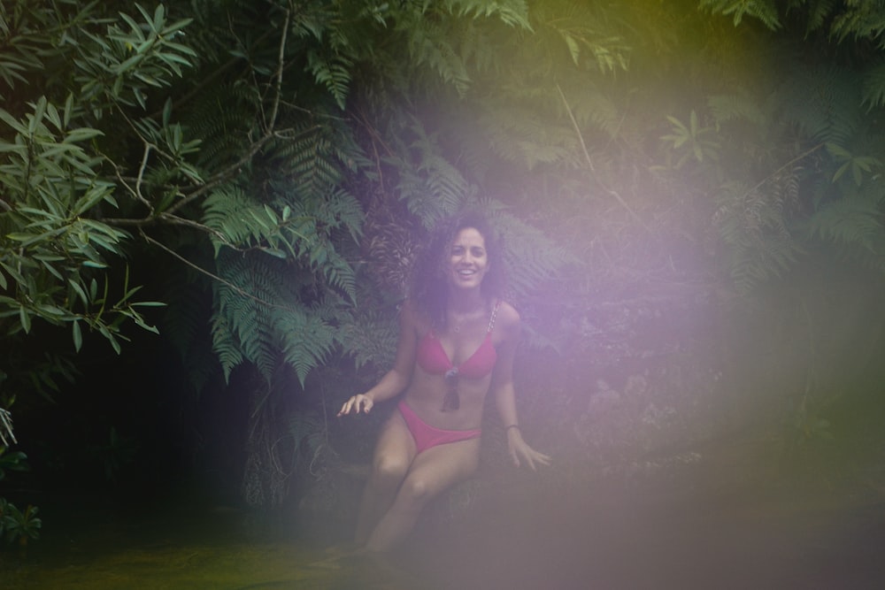 a woman in a red bikini sitting in the woods