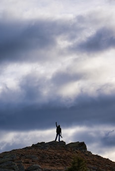 A smiling man standing outdoors at sunset, arms raised in accomplishment.