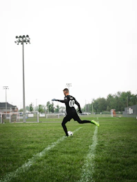 Cinematic shot of a male soccer player training intensely on a dimly lit pitch with neon green accents highlighting movement.