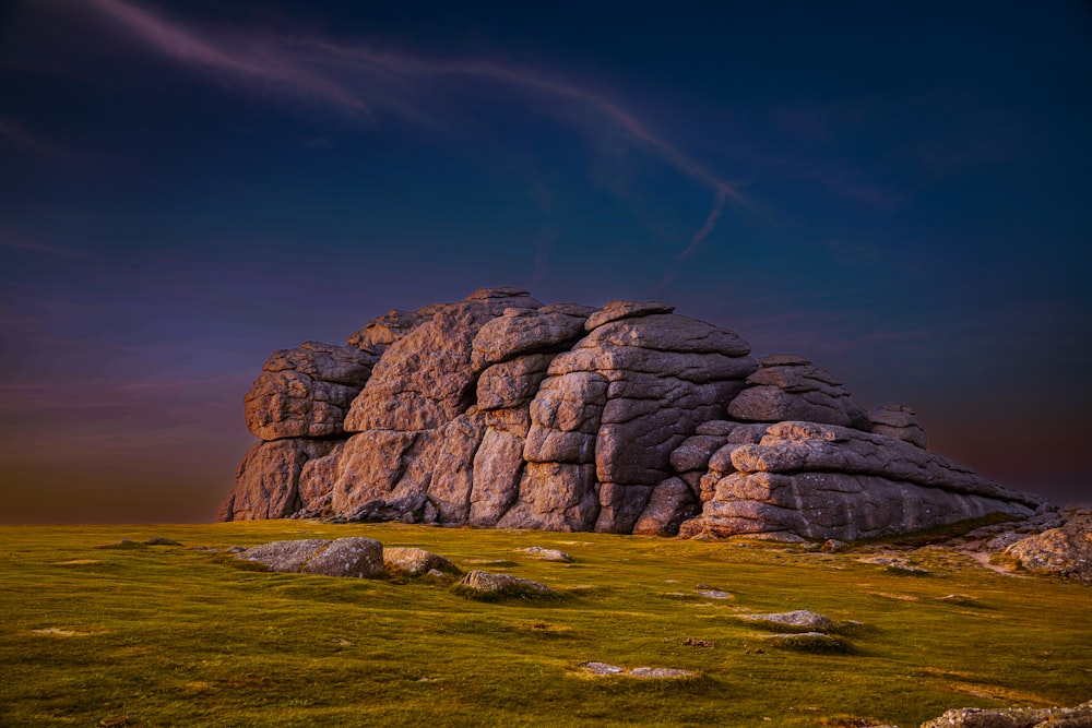 a large rock formation in the middle of a grassy field
