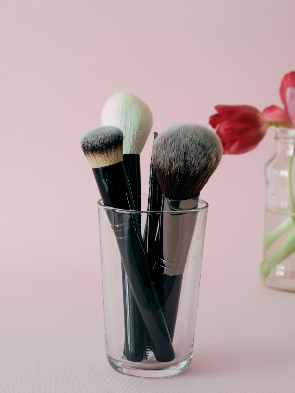 a glass filled with makeup brushes next to a vase with tulips