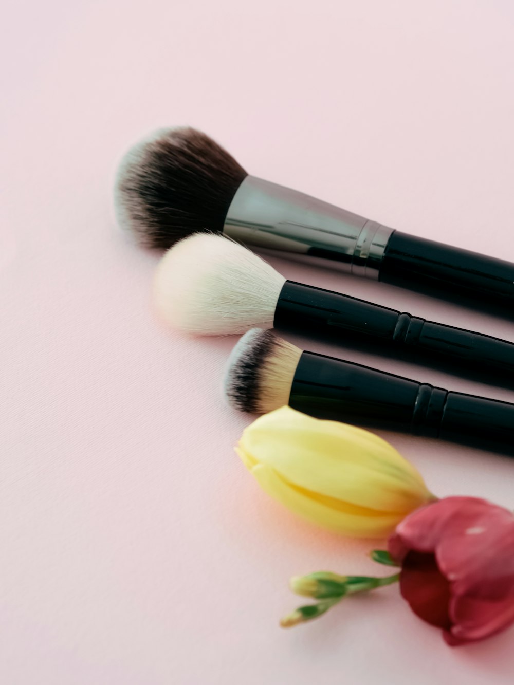 three makeup brushes sitting next to a flower