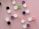 A collection of colorful contact lens cases is spread across a pink background. The cases come in pairs with two lids labeled 'L' and 'R'. They feature various colors such as black, green, purple, blue, and pink.