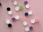 A collection of colorful contact lens cases is spread across a pink background. The cases come in pairs with two lids labeled 'L' and 'R'. They feature various colors such as black, green, purple, blue, and pink.