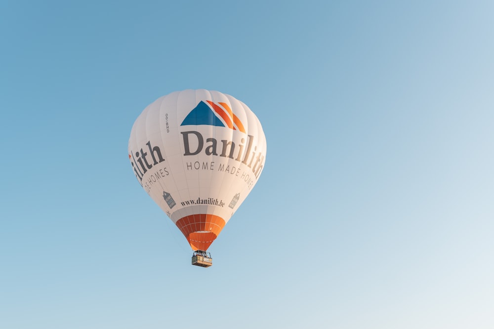 a white and orange hot air balloon flying through a blue sky