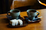 A rustic wooden table with several cups of Teh Manis Solo and traditional snacks.