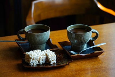 A rustic wooden table with several cups of Teh Manis Solo and traditional snacks.