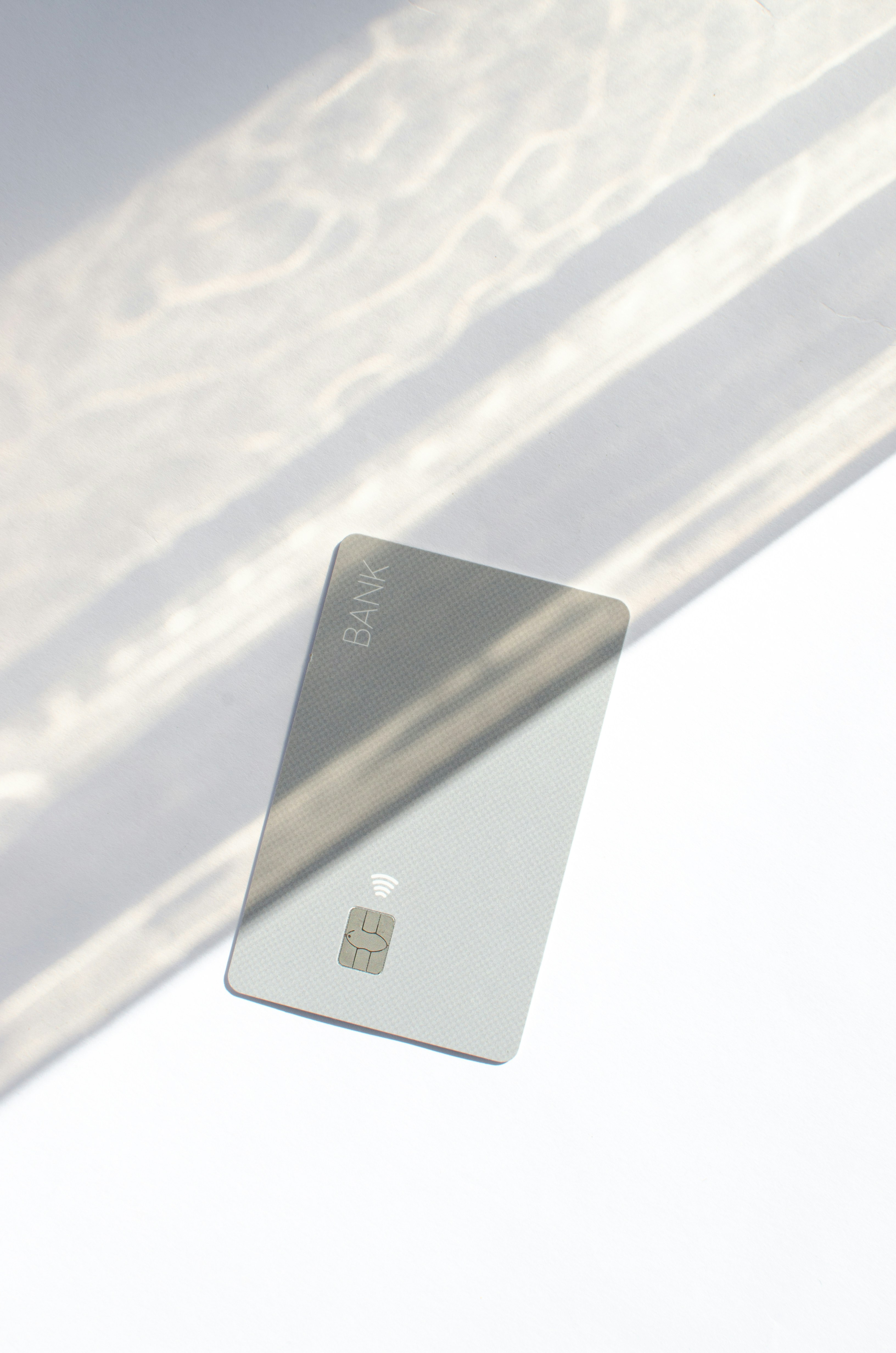 Plastic credit card with chip visible, on top of a table with soft lights and shadows. Gray card on white surface. Concept: finance, purchases, payments, loan, spending, investments and debts.