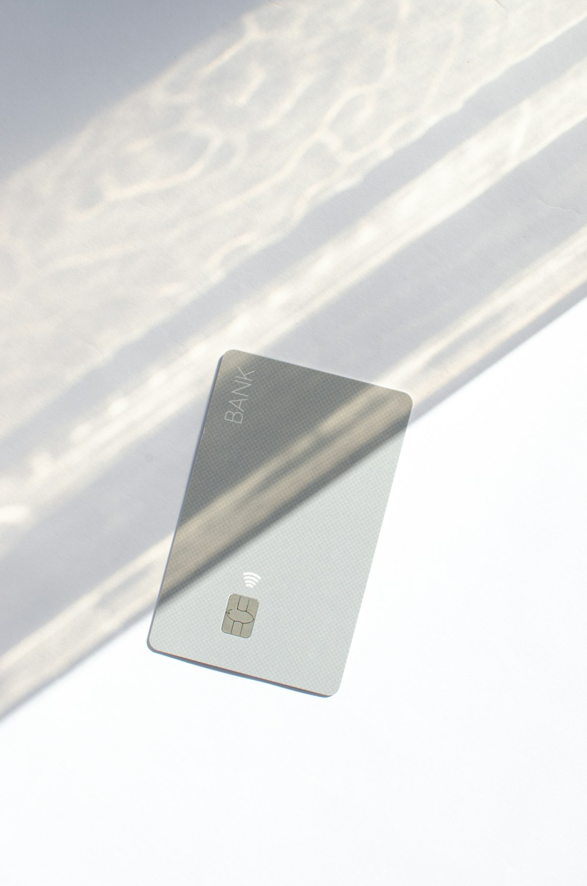 A minimalist silver bank card with chip and contactless icon on a softly lit white surface, credit-counseling register