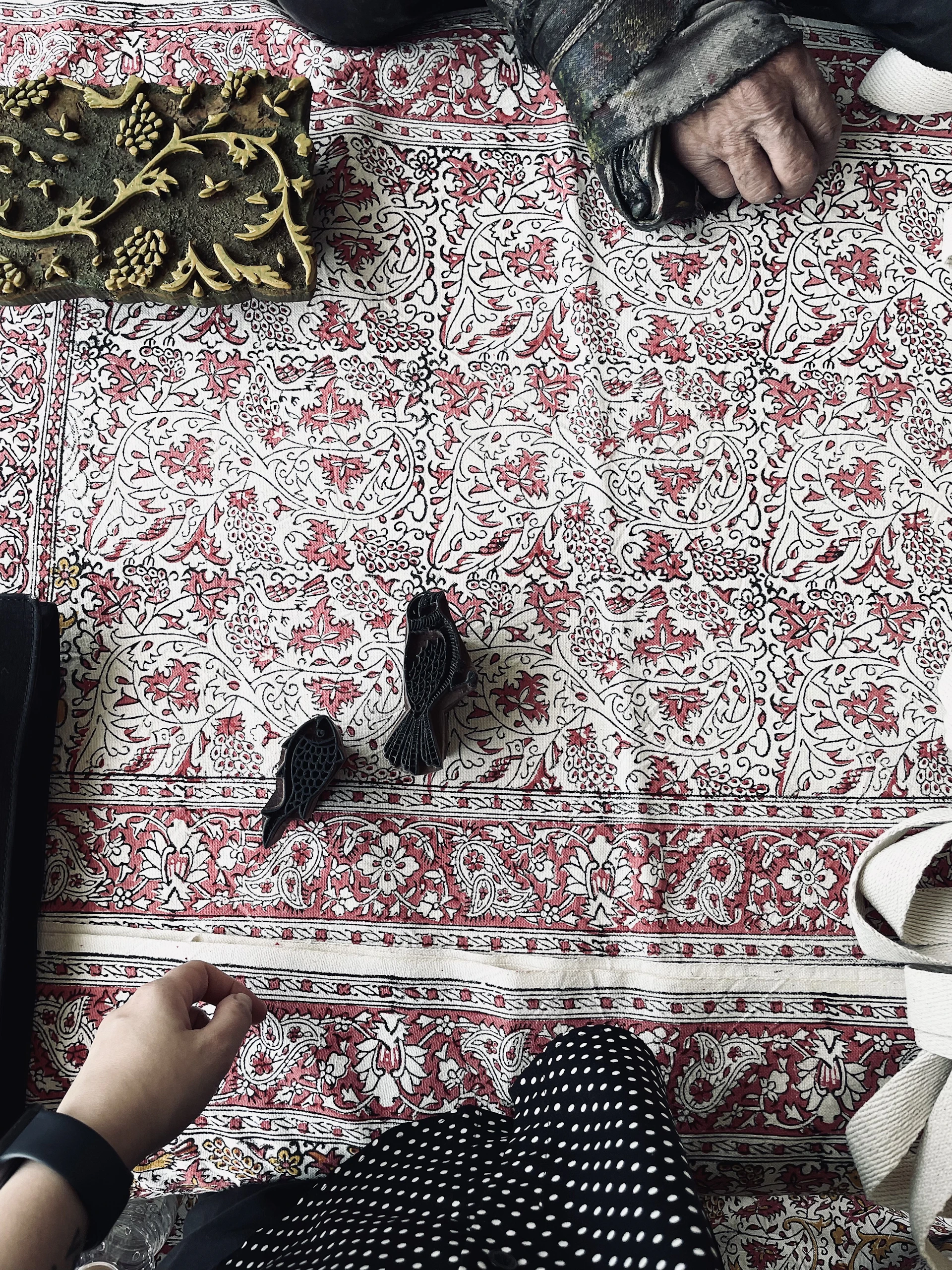An intimate moment of hands block printing intricate patterns on fabric, surrounded by scattered craft materials in moss green and burnt orange hues.