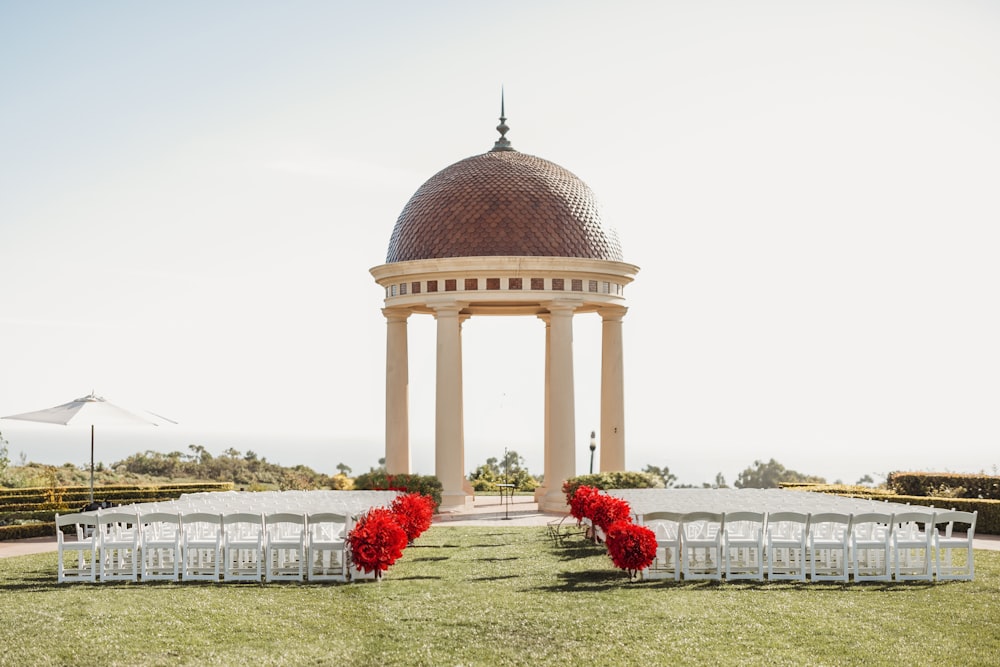 a gazebo with white chairs and red flowers in front of it