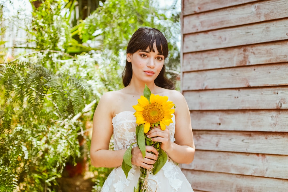 a woman in a wedding dress holding a sunflower