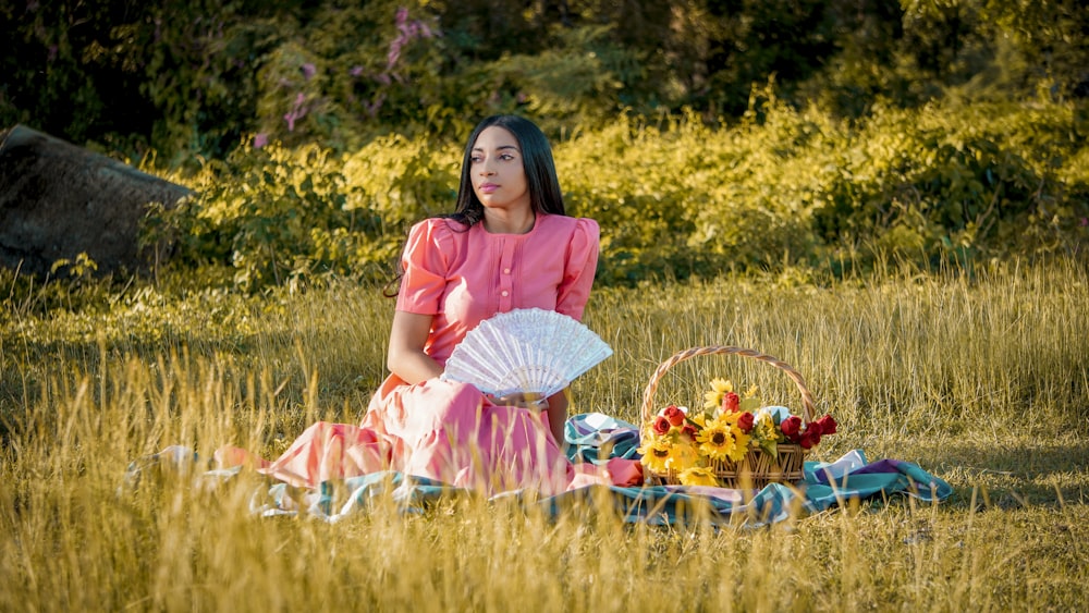 a woman sitting in a field with a basket of flowers
