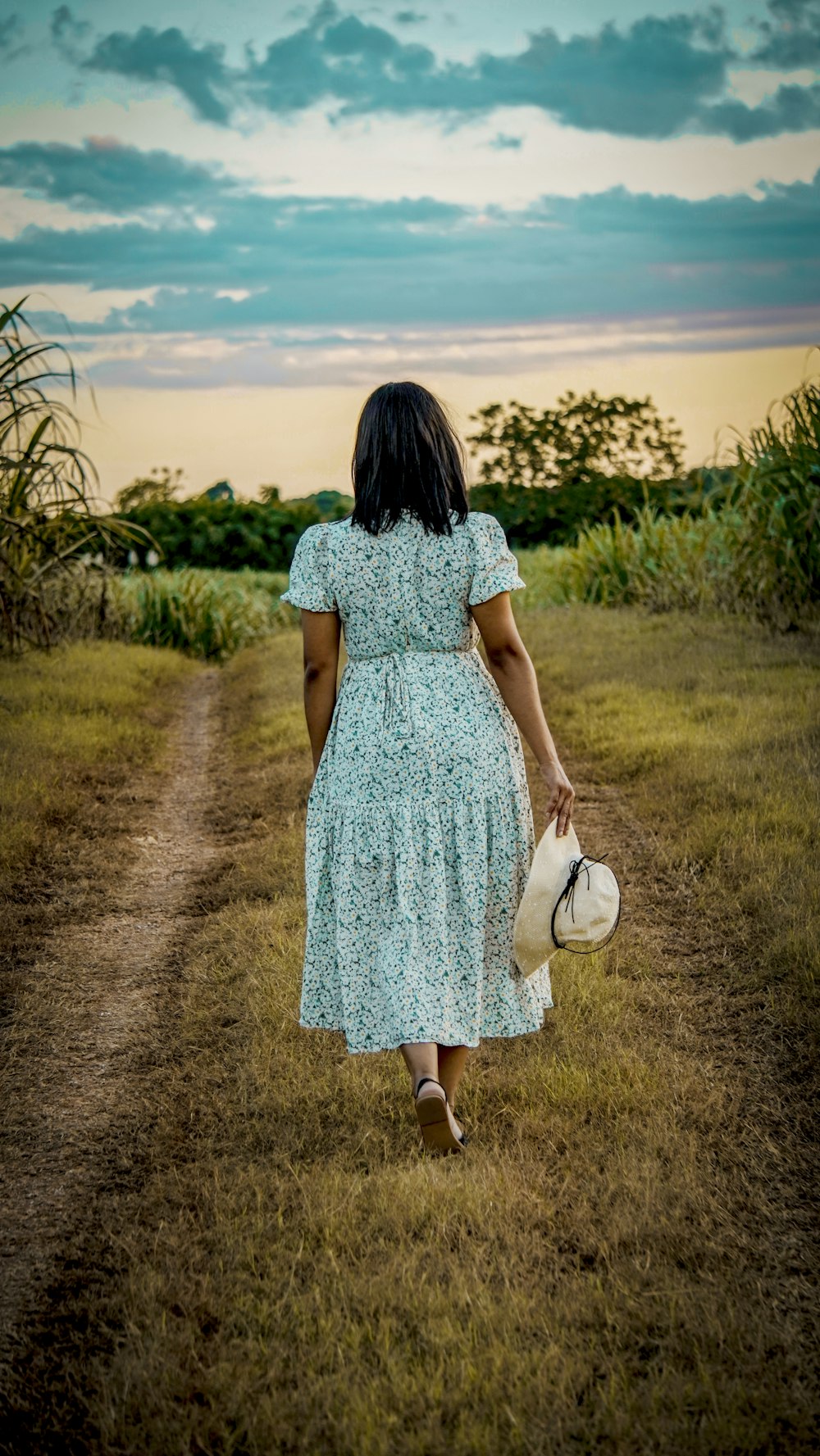 a woman in a dress walking down a dirt road