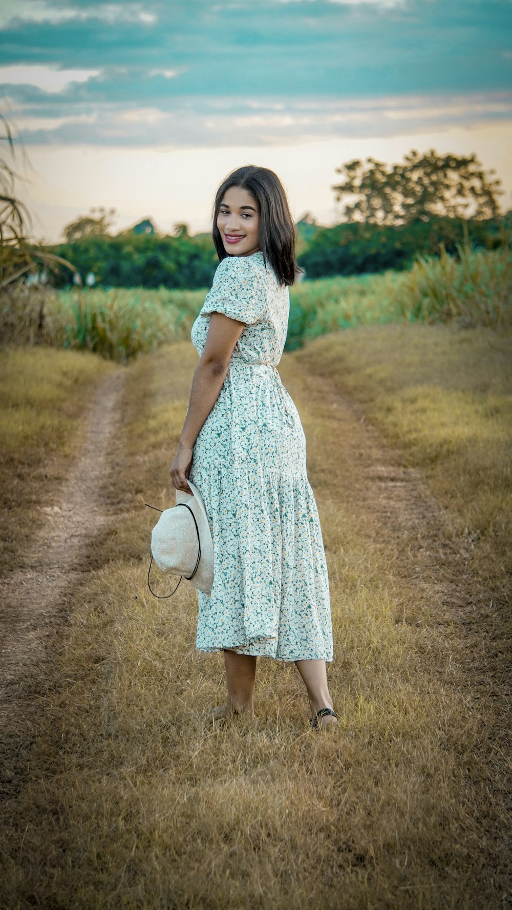 a woman in a dress and hat standing on a dirt road