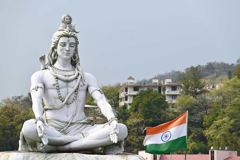 Una estatua de un hombre sentado en posición de loto con una bandera frente a