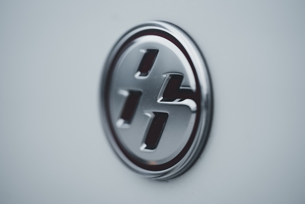 A close-up of a metallic, circular emblem on a light-colored surface, featuring a stylized letter design.