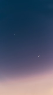 A serene sky with a small crescent moon and a bright star visible against a smooth gradient from deep blue to soft pink.