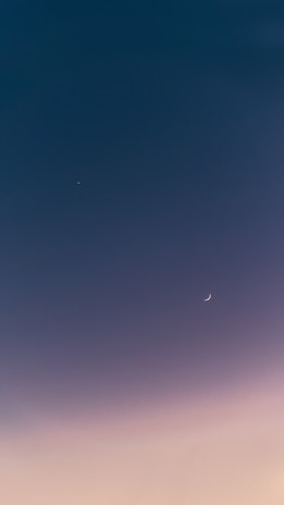 A serene sky with a small crescent moon and a bright star visible against a smooth gradient from deep blue to soft pink.