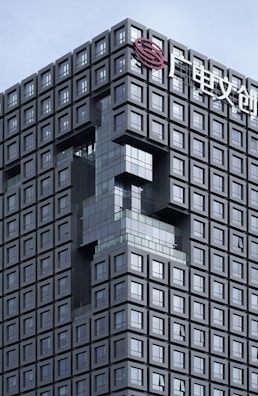 A modern architectural building with a grid-like design composed of numerous square windows. There is an artistic indentation in the facade forming an abstract shape, and a logo with Chinese characters is seen at the top.