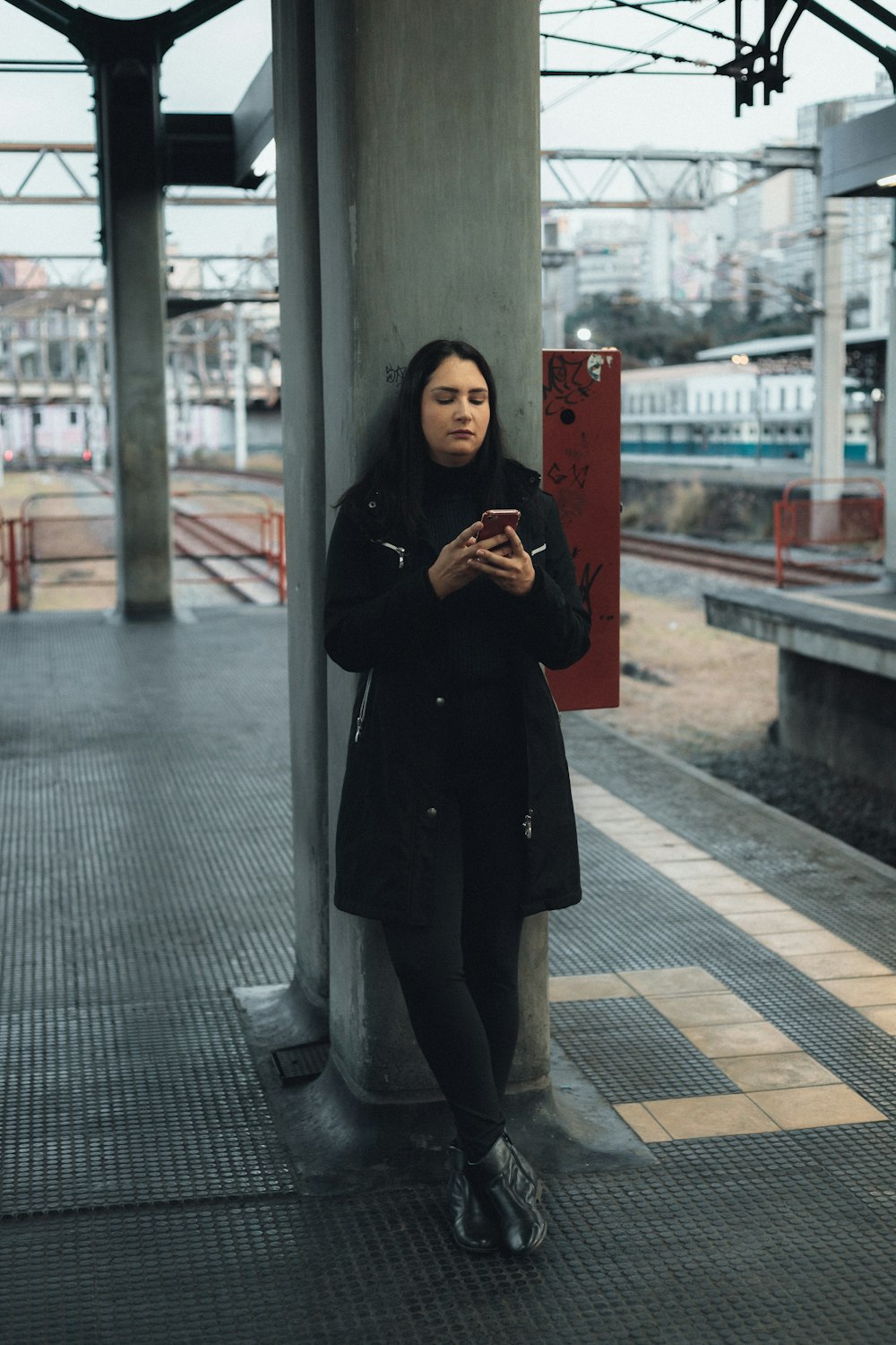 a woman standing on a train platform looking at her phone