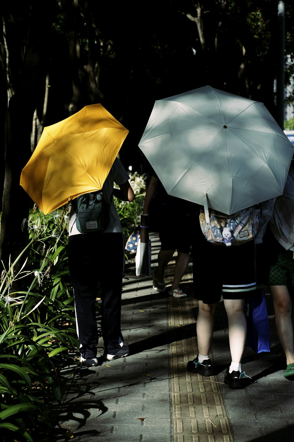 eine gruppe von menschen, die einen bürgersteig hinuntergehen, regenschirme halten