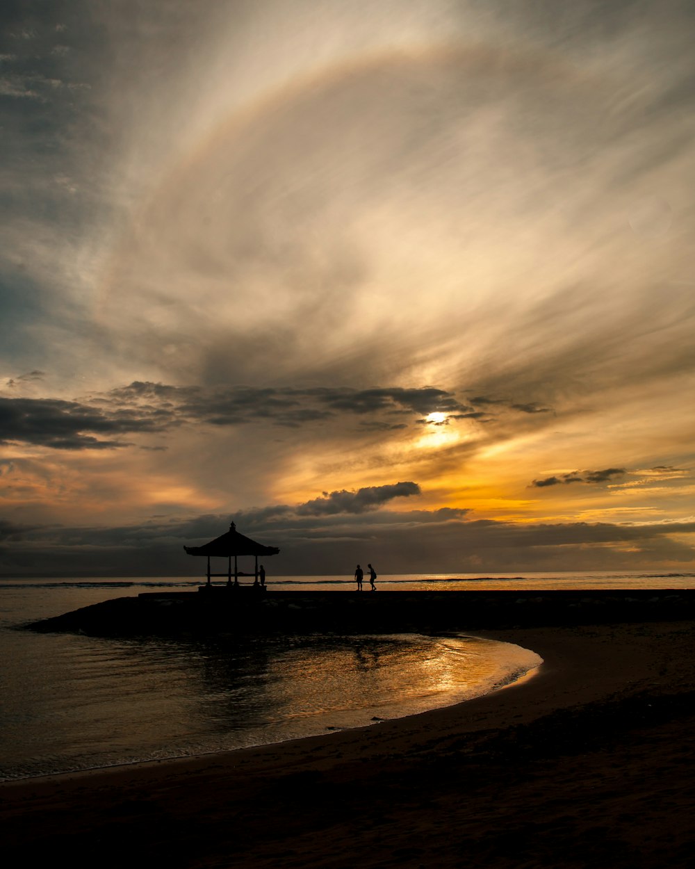 a couple of people standing on top of a beach under a cloudy sky