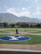 A vibrant softball game in progress with players wearing rainbow-colored jerseys under a clear Denver sky.