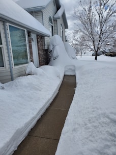 Snow being cleared from a cozy residential driveway covered in fresh snow.