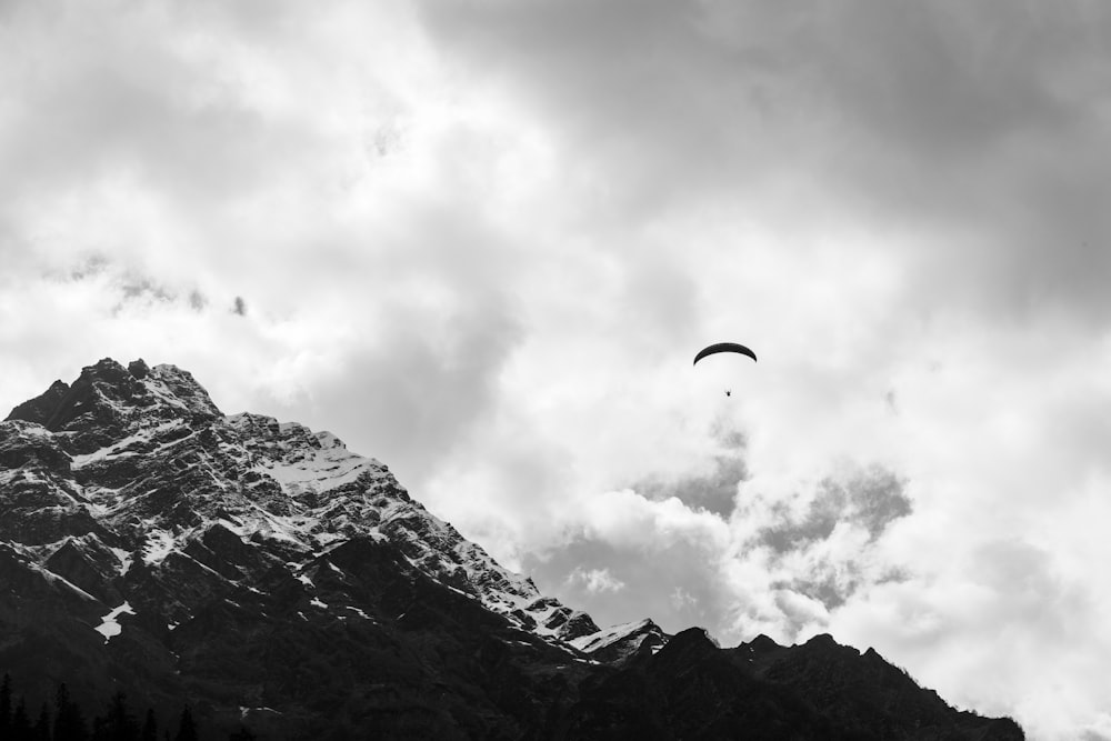 a paraglider flying over a mountain under a cloudy sky