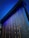 A modern architectural installation featuring a large, vertical panel with cascading water illuminated by blue lights. The panel appears to have a textured surface, and the lighting creates a vibrant contrast against the dark background.