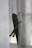 A large green grasshopper clings to a sheer white curtain, its long legs and antennae prominently visible. The natural lighting illuminates the insect's textured body and wings.