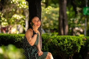 A woman in a vibrant dress smiling while enjoying a sunny day in the park.