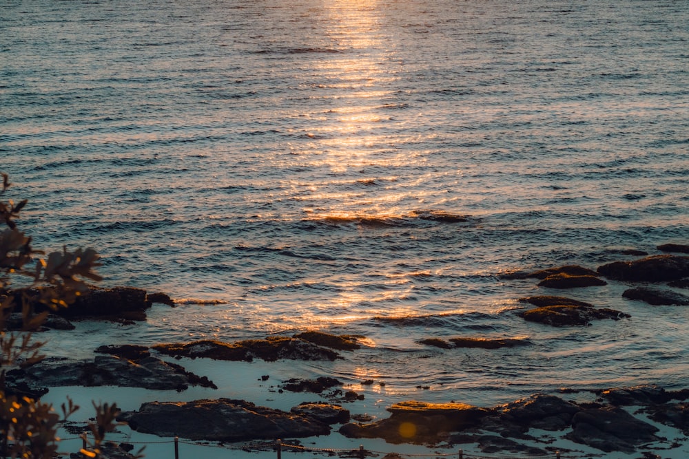 the sun is setting over the ocean with rocks in the foreground