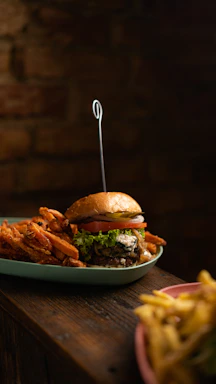 A beautifully plated gourmet burger with fresh greens and a side of crispy fries on a rustic wooden table.