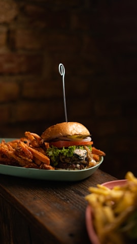 A vibrant, colorful vegan burger with fresh greens and a side of crispy sweet potato fries on a rustic wooden table.
