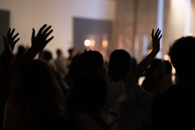 A diverse group of people raising hands in worship under soft, warm lighting.