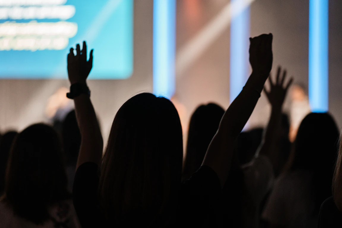 Close-up of hands raised in worship with bright stage lights in the background