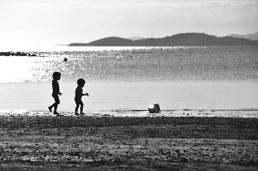 Kids playing on a sandy beach with colorful buckets and a bright blue sky overhead.
