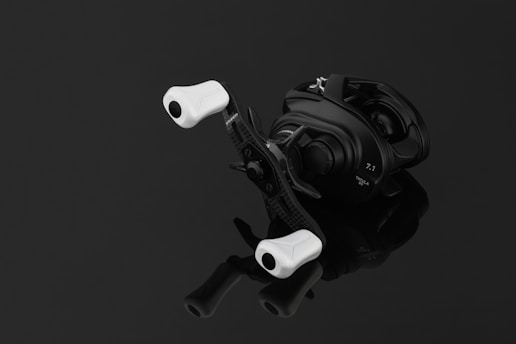 A sleek, light-colored fishing reel resting on a wooden dock with a calm lake in the background.