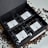 A neatly arranged black gift box containing four packages of coffee, labeled from TOH #1 to TOH #4. Each package has a white label with text and a QR code. Coffee beans are scattered around the box on a white surface.