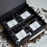 A neatly arranged black gift box containing four packages of coffee, labeled from TOH #1 to TOH #4. Each package has a white label with text and a QR code. Coffee beans are scattered around the box on a white surface.