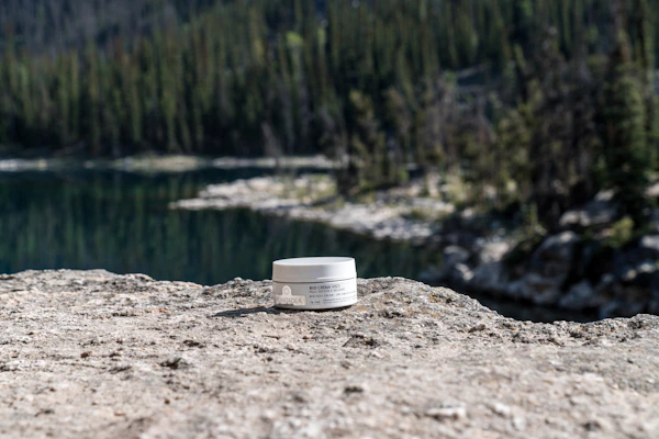 A soothing lotion jar resting on smooth stones beside a calm pool reflecting sunlight.