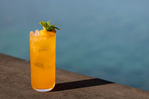 A vibrant glass of freshly squeezed orange juice with ice and mint leaves on a wooden table