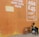 A boy sits on the ground against an orange wall, petting a dog. Another dog is nearby, and a soccer ball is next to them. The wall has an advertisement for airtime and data.