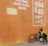 A boy sits on the ground against an orange wall, petting a dog. Another dog is nearby, and a soccer ball is next to them. The wall has an advertisement for airtime and data.