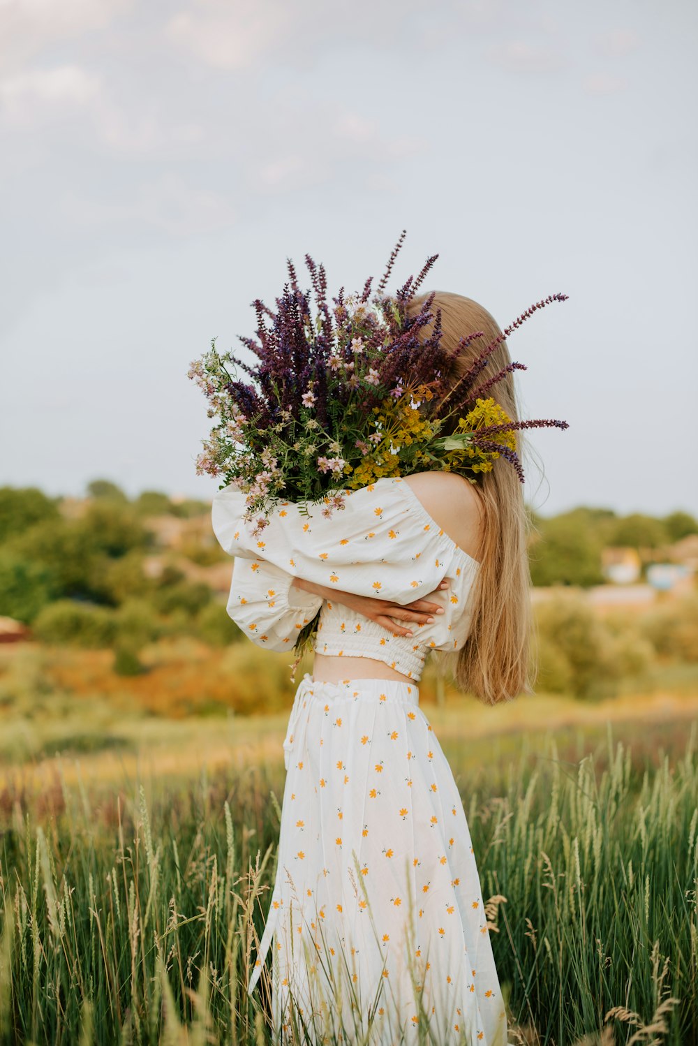 a woman standing in a field holding a bouquet of flowers
